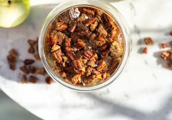 Individual apple crumbles topped with browned crumbs and pecans, with green apples on a marble table