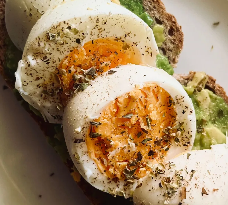 Avocado toast with sliced boiled eggs and a light herb seasoning on a white plate