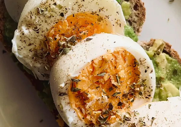 Avocado toast with sliced boiled eggs and a light herb seasoning on a white plate