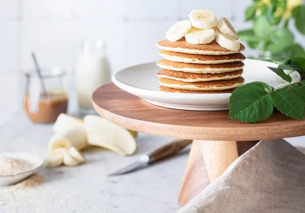 Golden pancakes stacked on a white plate and topped with fresh banana slices