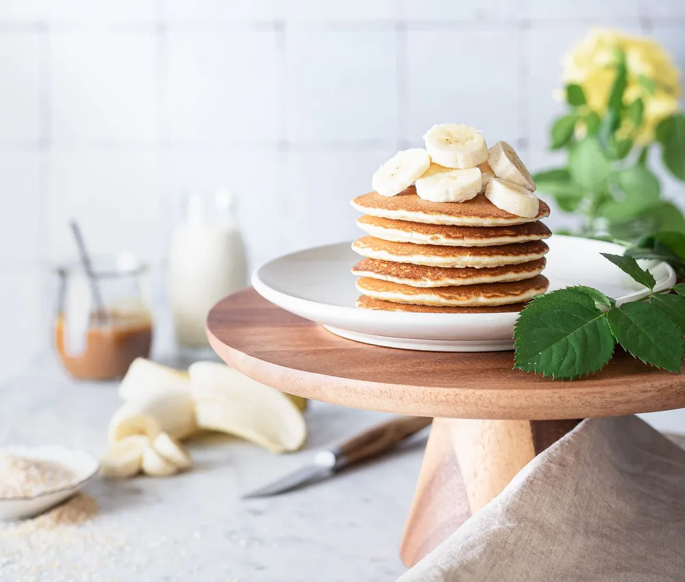 Golden pancakes stacked on a white plate and topped with fresh banana slices