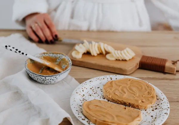 Peanut butter toast with sliced banana on the board behind it