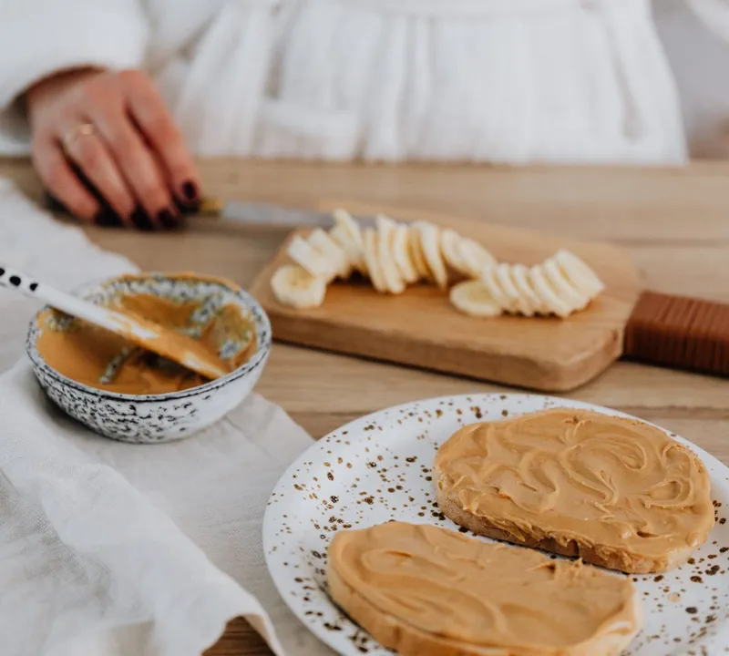 Peanut butter toast with sliced banana on the board behind it