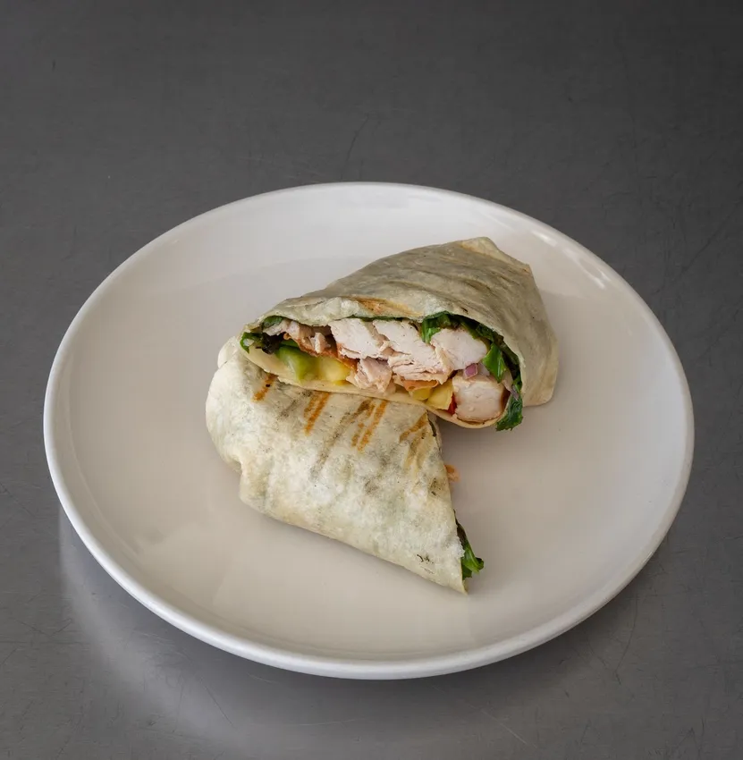 Toasted chicken wrap cut in two on a white plate, with visible chicken pieces and fresh salad