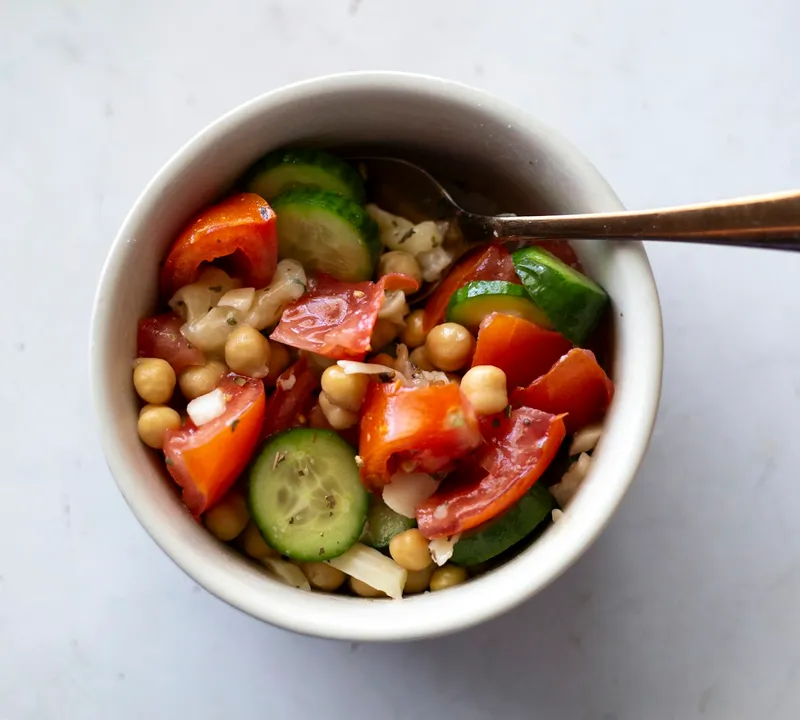 Chickpeas, cucumber and tomatoes in a white bowl with a spoon