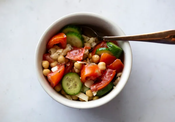 Chickpeas, cucumber and tomatoes in a white bowl with a spoon