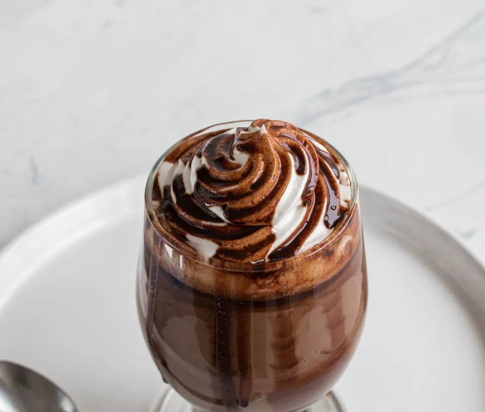 Chocolate dessert in a glass on a white plate with a cream and chocolate swirl