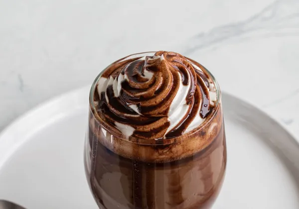 Chocolate dessert in a glass on a white plate with a cream and chocolate swirl