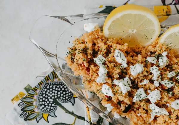 Tomato-coloured couscous topped with crumbled cheese and lemon wedges