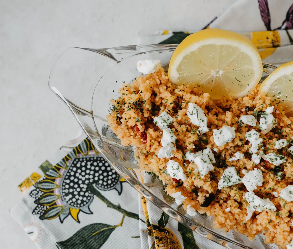 Tomato-coloured couscous topped with crumbled cheese and lemon wedges