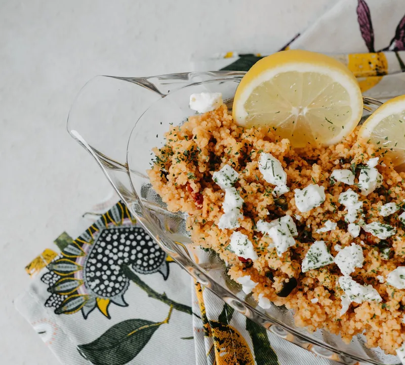 Tomato-coloured couscous topped with crumbled cheese and lemon wedges