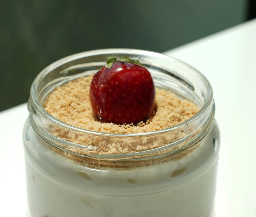 Strawberry cheesecake in a glass jar with biscuit crumbs and a strawberry on top