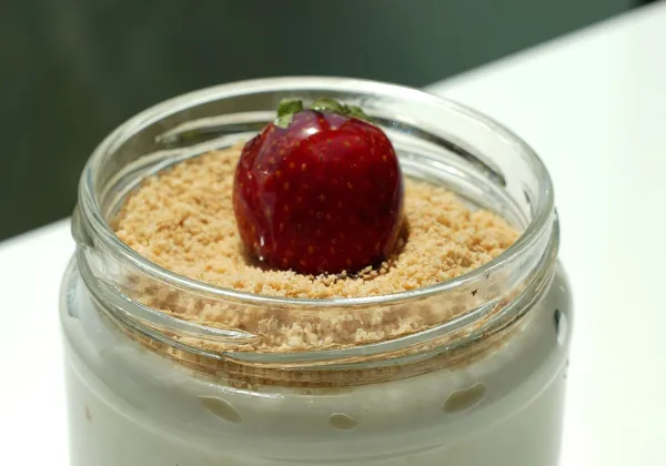 Strawberry cheesecake in a glass jar with biscuit crumbs and a strawberry on top