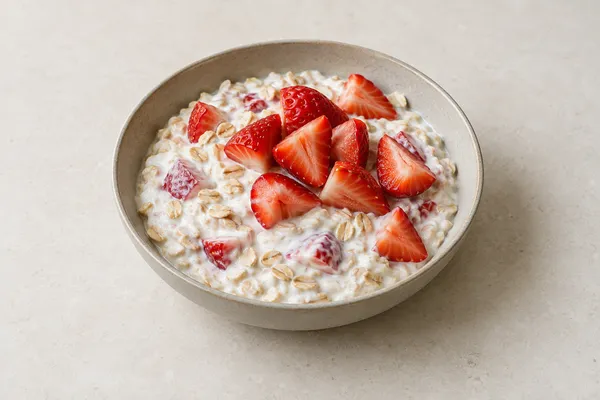 Fresh strawberry quarters over Greek yogurt and softened oats in a ceramic bowl