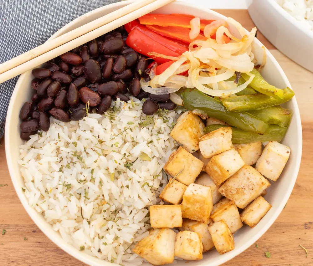 A bowl of rice with tofu cubes, black beans, peppers and onion