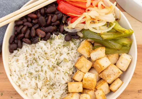 A bowl of rice with tofu cubes, black beans, peppers and onion