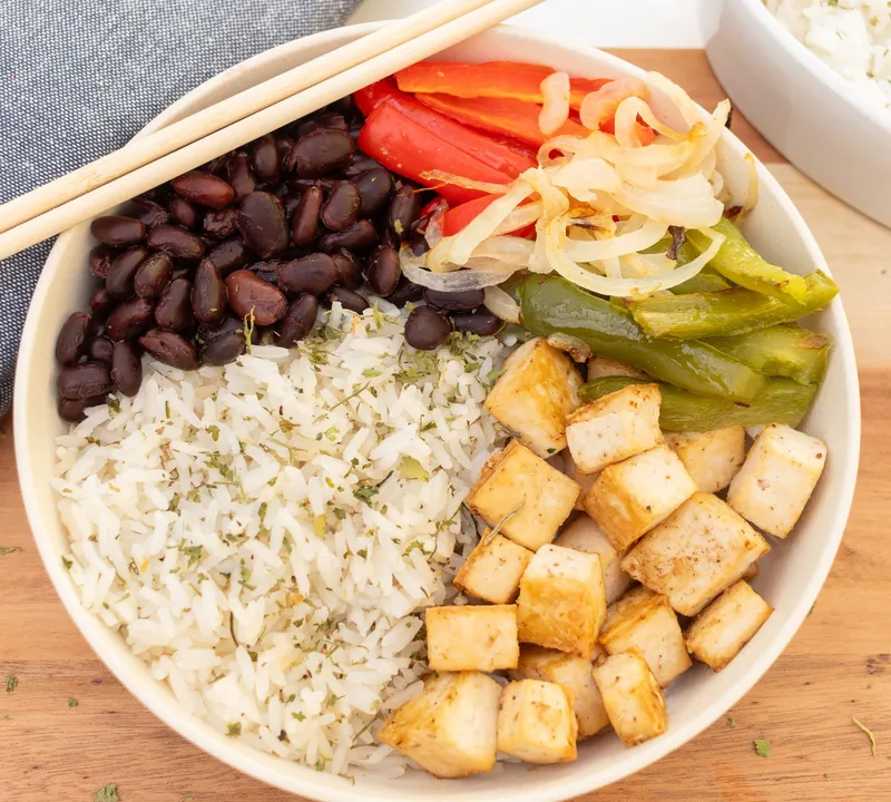 A bowl of rice with tofu cubes, black beans, peppers and onion
