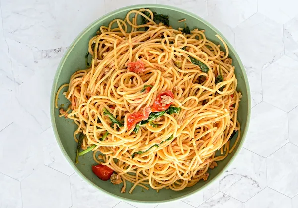 Spaghetti with tomatoes and leafy greens on a green plate against a light background