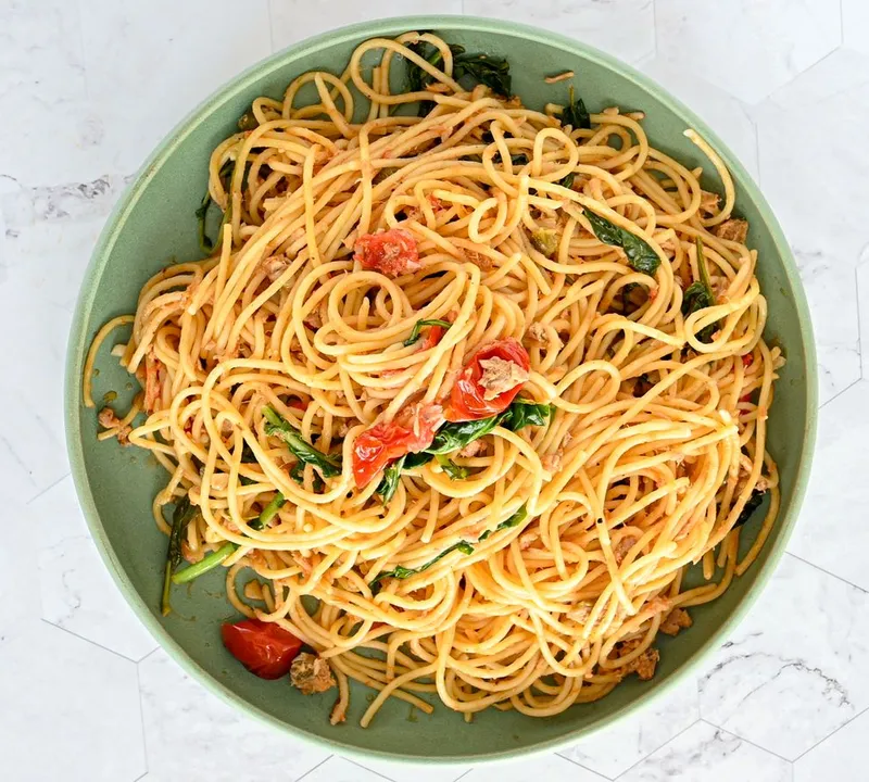 Spaghetti with tomatoes and leafy greens on a green plate against a light background