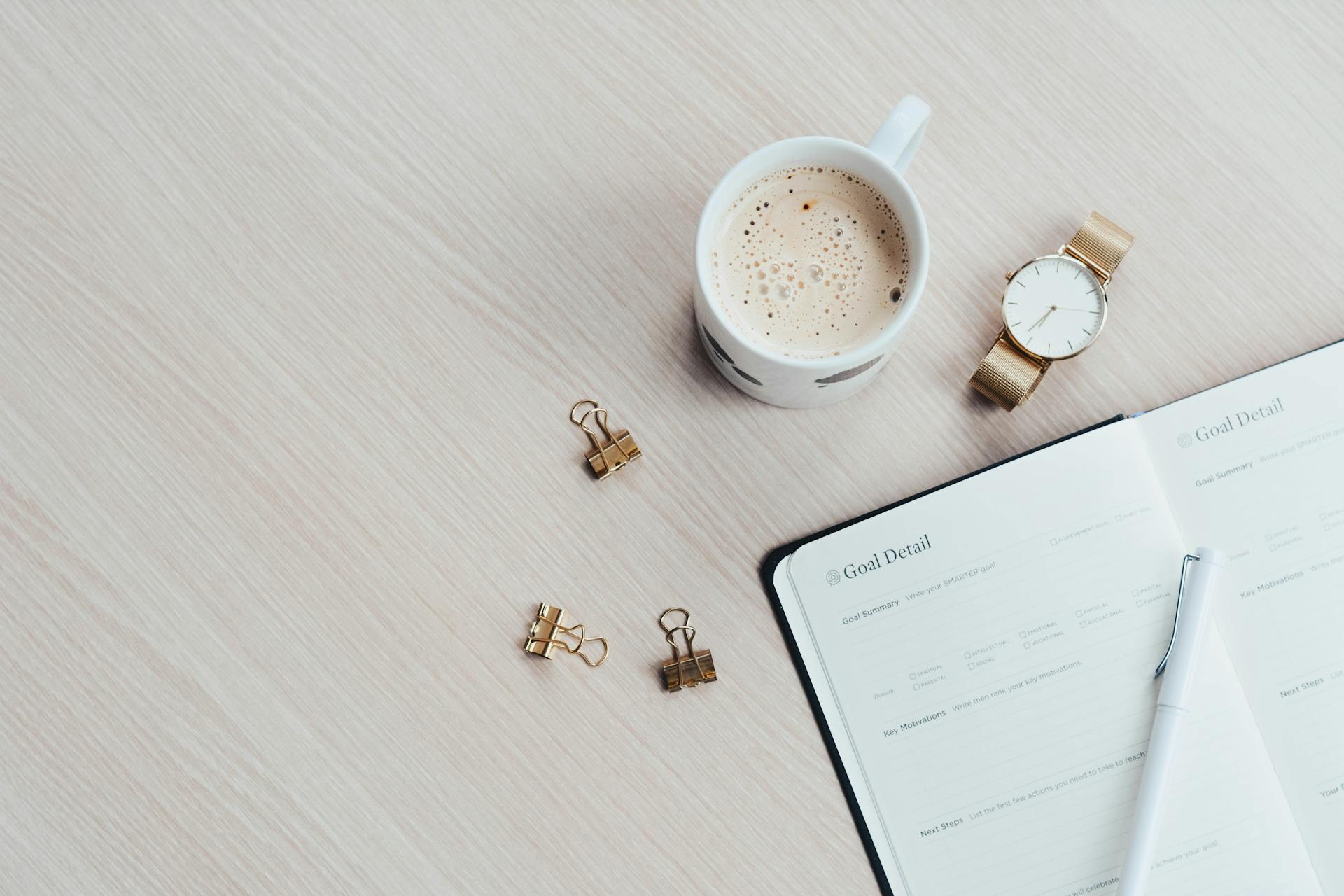 An open planner, a pen and a cup of coffee