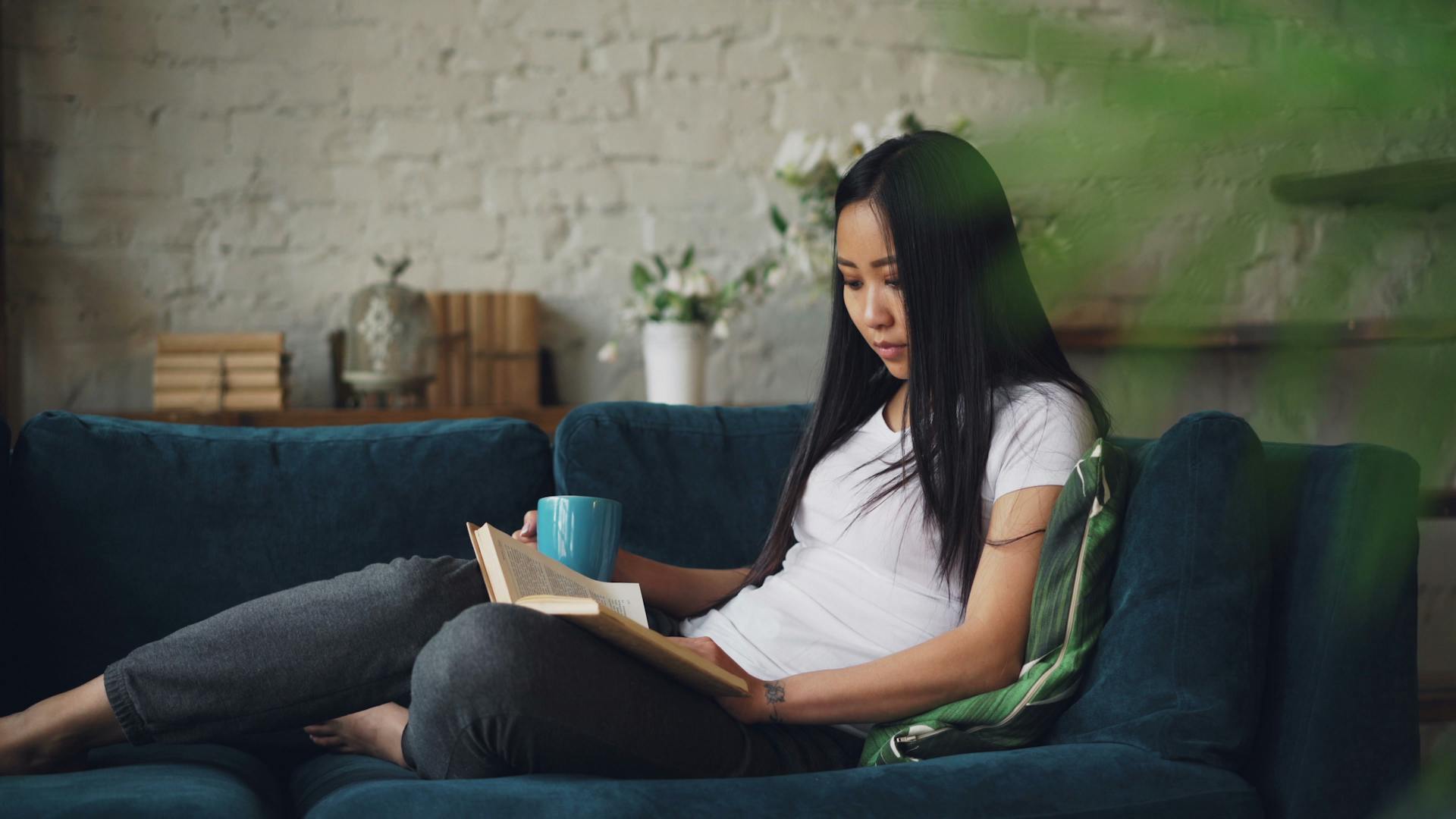 A woman reading on a sofa beside a window