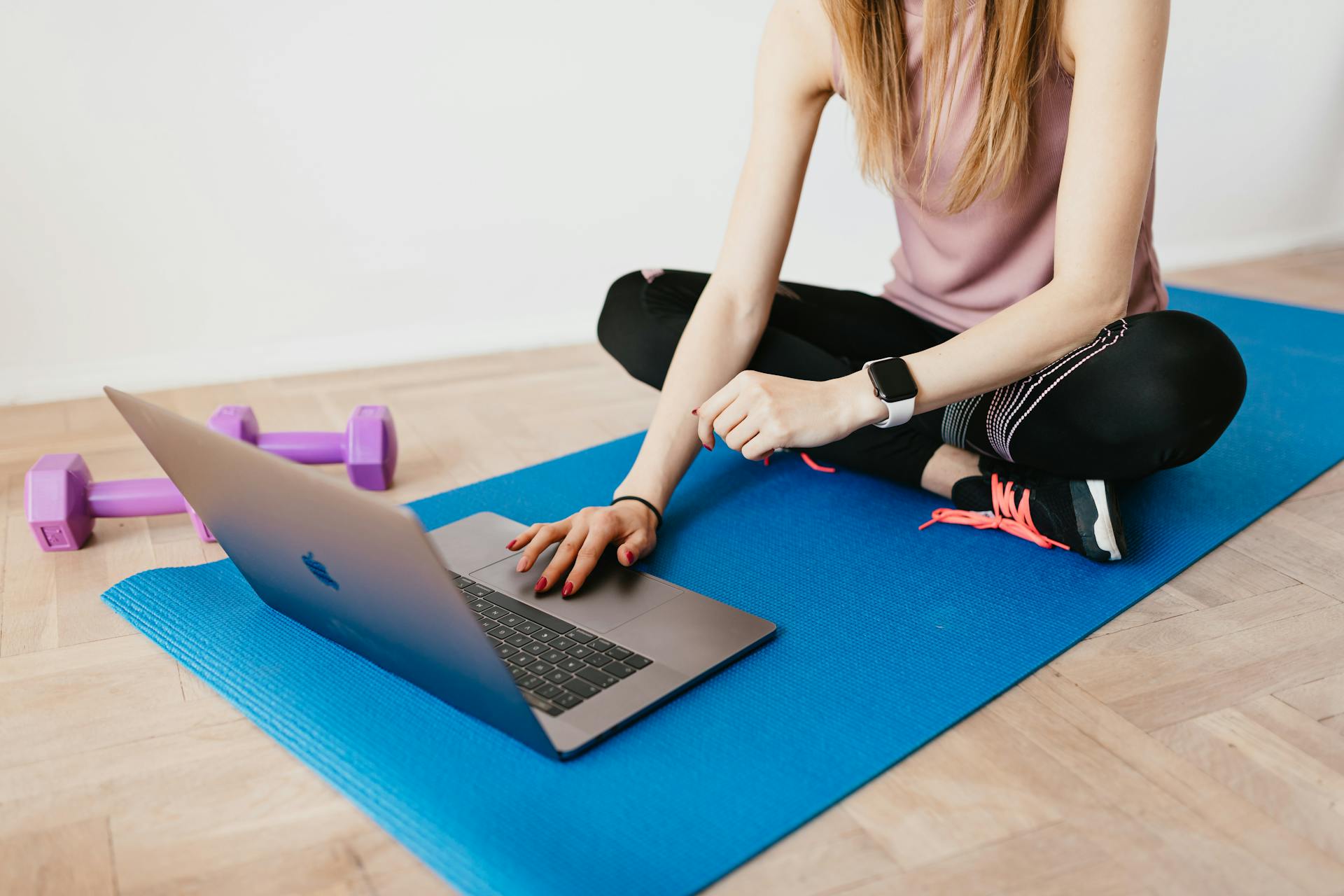 A woman setting up a home workout with a mat, dumbbells and a laptop